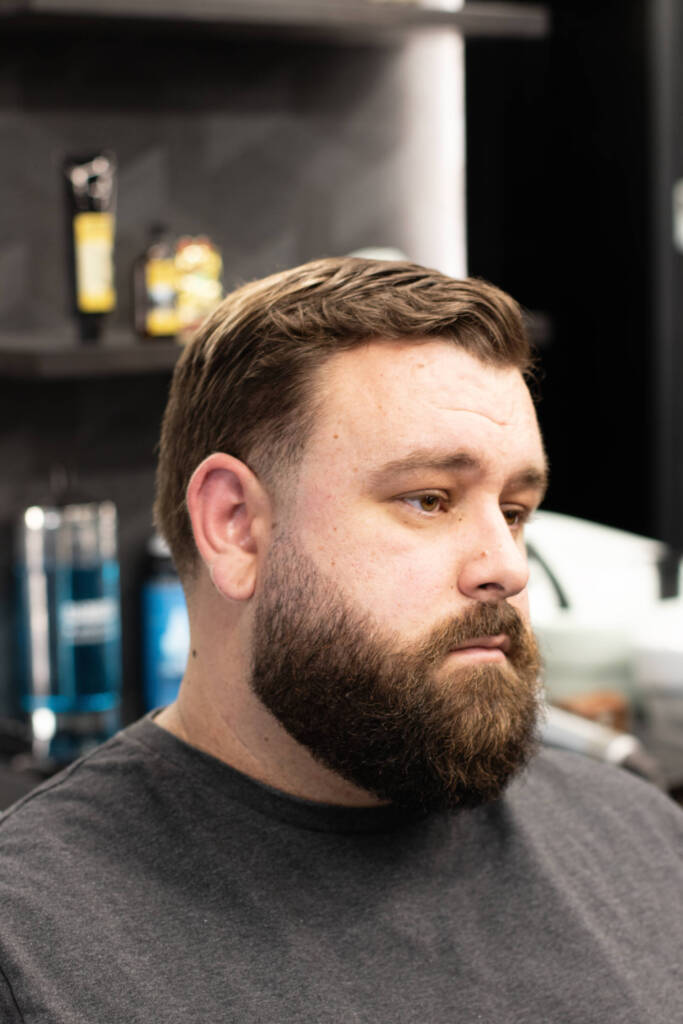 Close-up of a man with a neatly styled taper fade haircut and sharply groomed full beard, captured inside Varndells barbershop.